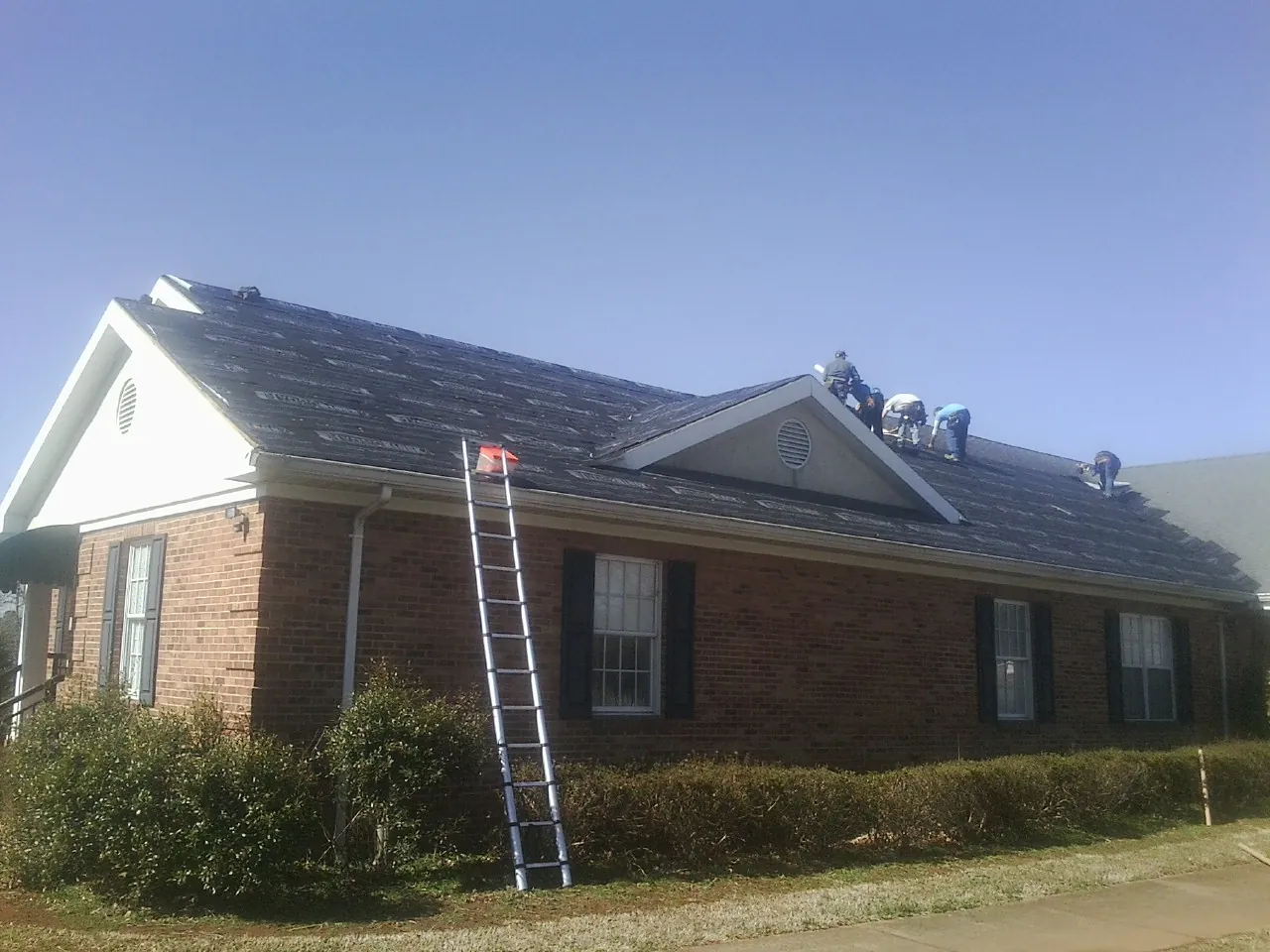 Crew tearing shingles off a brick ranch roof with a ladder set — Metal Roof Repair work by our crew in Hackleburg