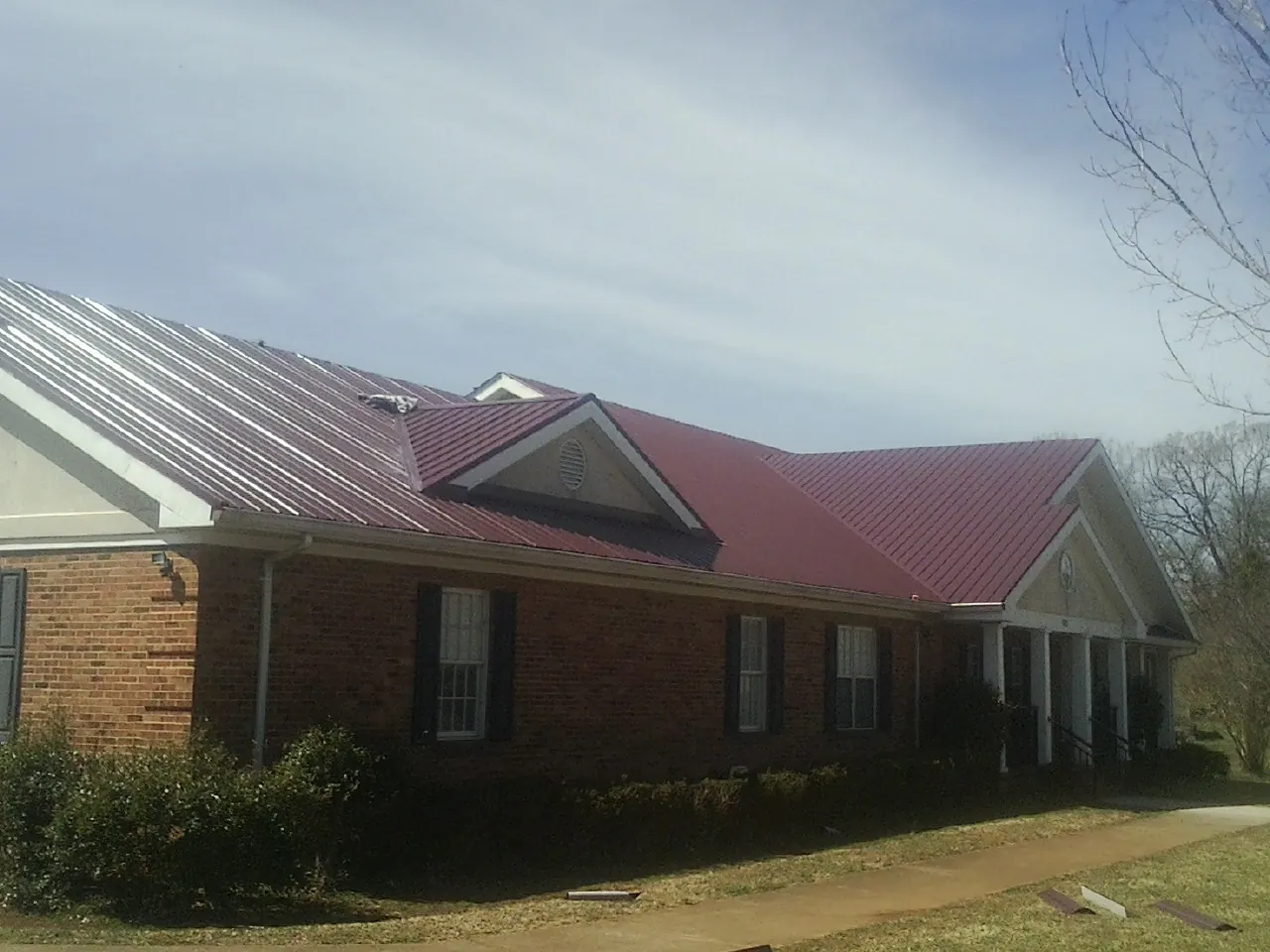 Red metal roof with gabled entries on a long brick building, from a Hail Damage Roof Repair job in Hackleburg