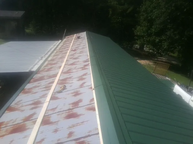Old rusted panels beside newly installed green metal roofing — Wind Damage Roof Repair by Roofing Brothers in Hackleburg