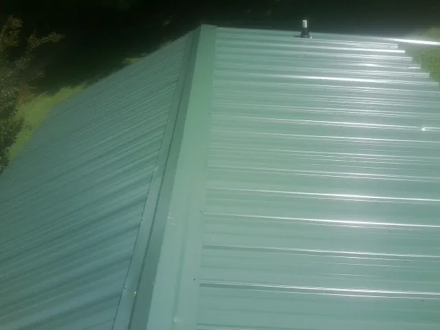 New green metal panels meeting at the ridge of a roof — Flat Roof Repair work by our crew in Hackleburg