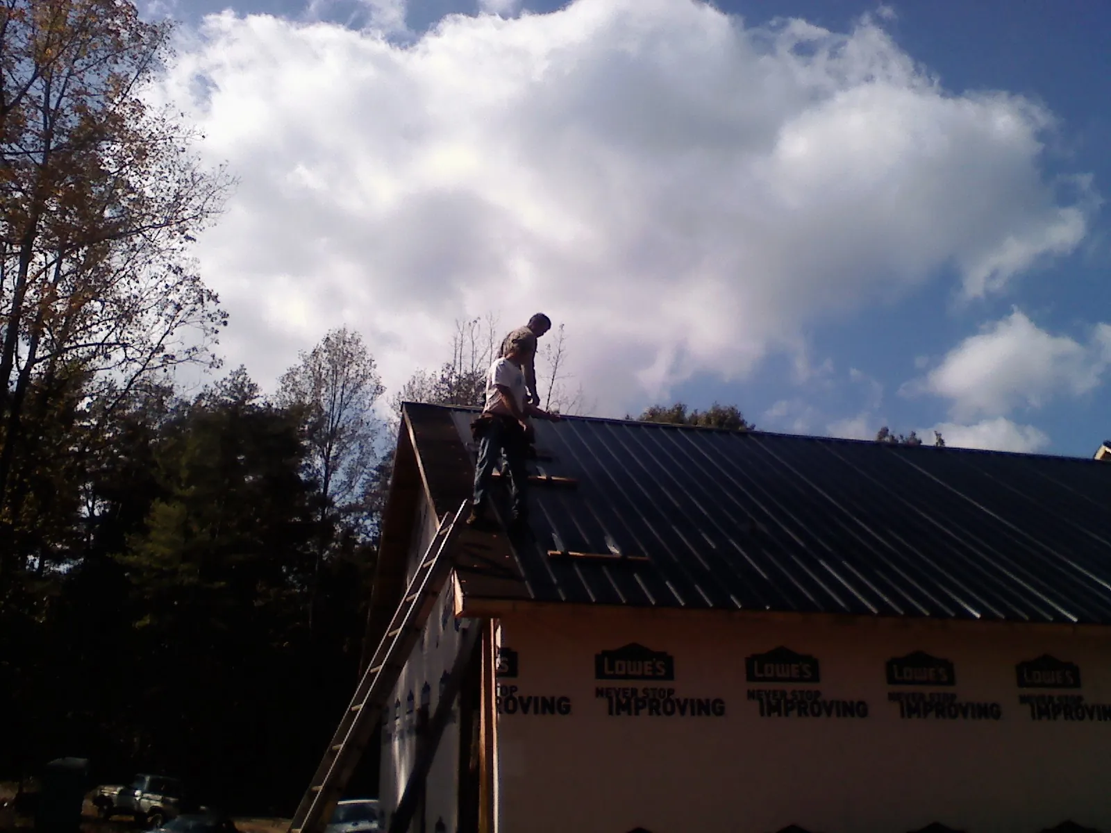 Roofer fastening dark metal panels high against a cloudy sky, from a Roof Inspection job in Hackleburg