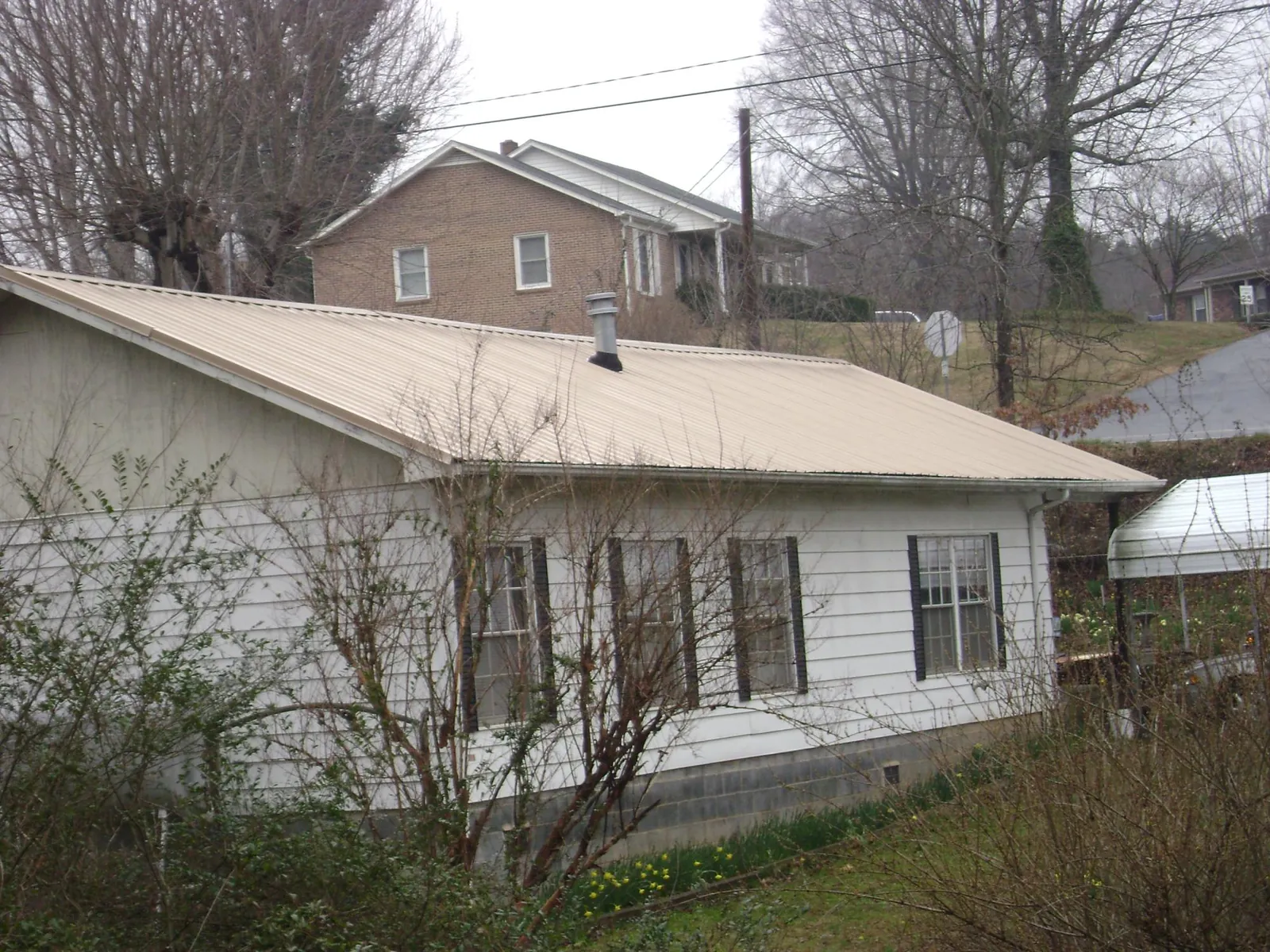 Tan metal roof on a white sided house set into a hillside — Commercial Roofing by Roofing Brothers in Hackleburg