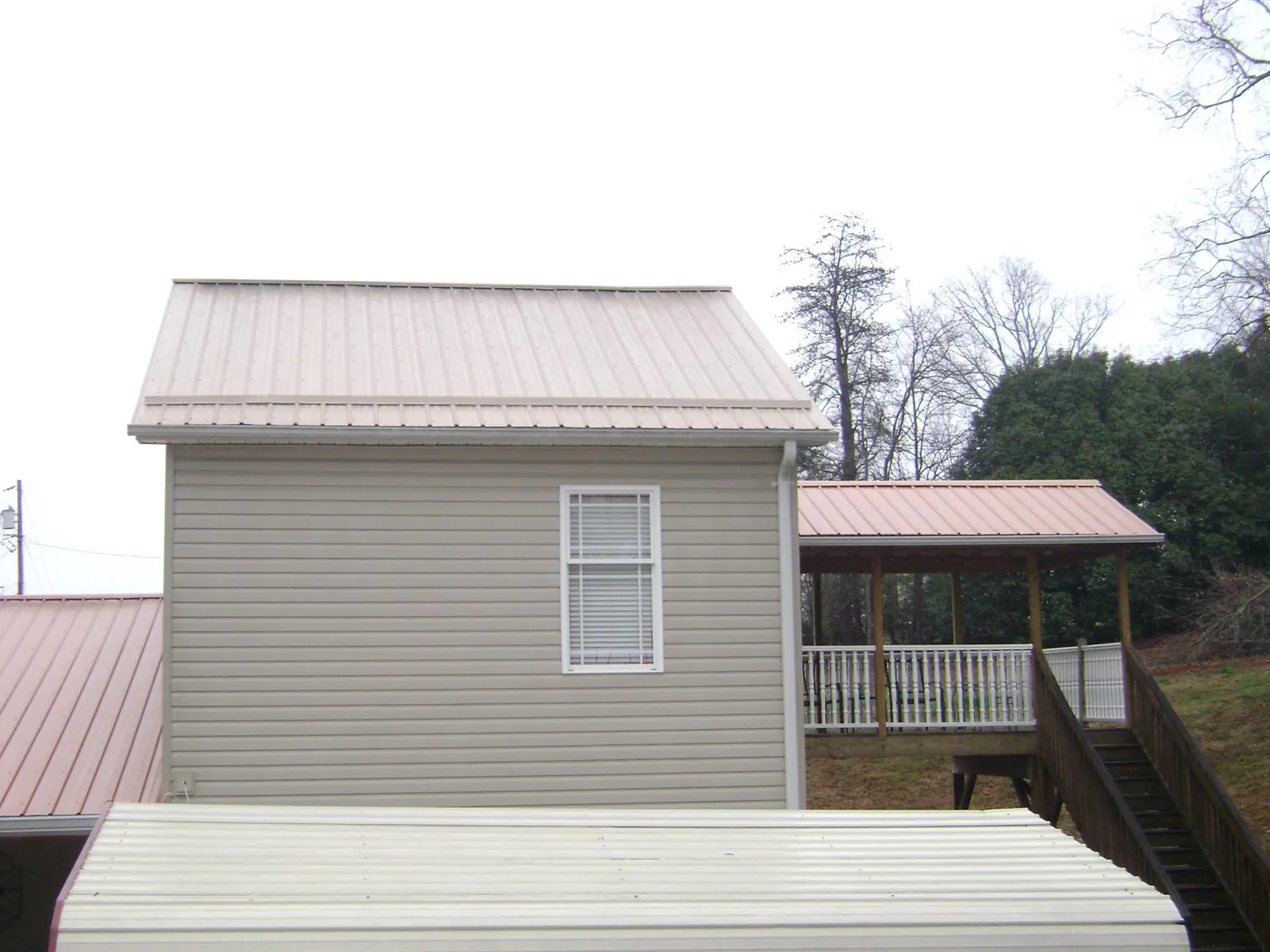 Tan metal roofs on a two story addition and attached porch, from a Roof Replacement job in Hackleburg